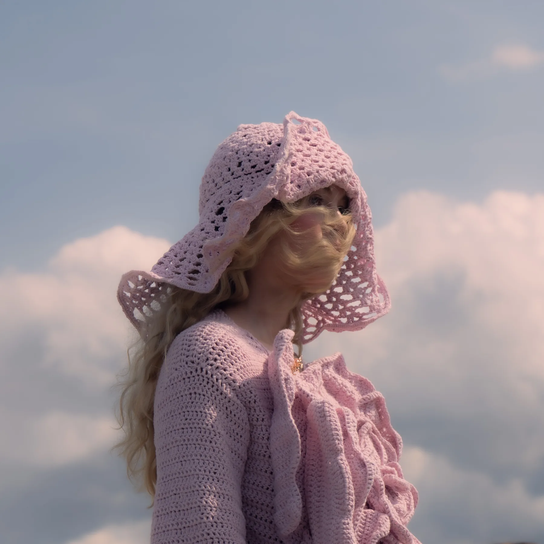 Pioni Jacket with its crocheted headpiece, pink, against the sky on the runway